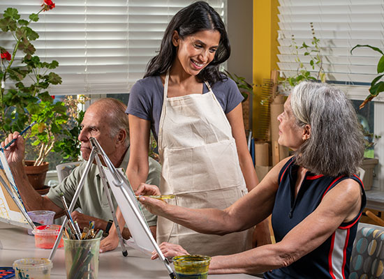 Group of older adults painting while instructor talks with a woman in the class.